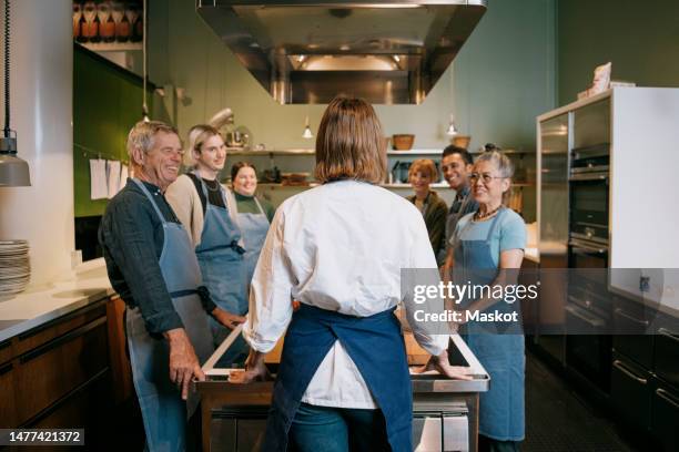 rear view of female chef briefing multiracial students standing in kitchen - chef demonstration stock pictures, royalty-free photos & images