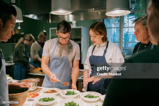 female chef assisting male student during cooking class in kitchen - cooking class stock pictures, royalty-free photos & images