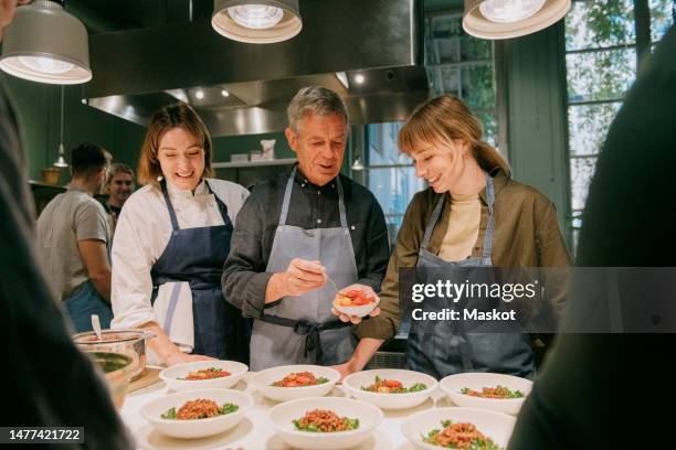 smiling female chef with students plating during cooking class in kitchen - garniture végétale photos et images de collection
