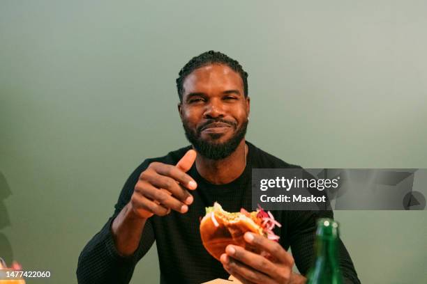 portrait of smiling man eating burger at restaurant - man holding a burger stock pictures, royalty-free photos & images