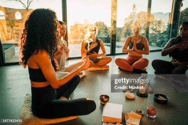 woman holding burning sandalwood while meditating with female friends at retreat center - new age stock pictures, royalty-free photos & images