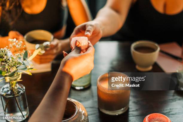 hand of woman passing crystal to female friend over burning candle at retreat center - new age stock pictures, royalty-free photos & images