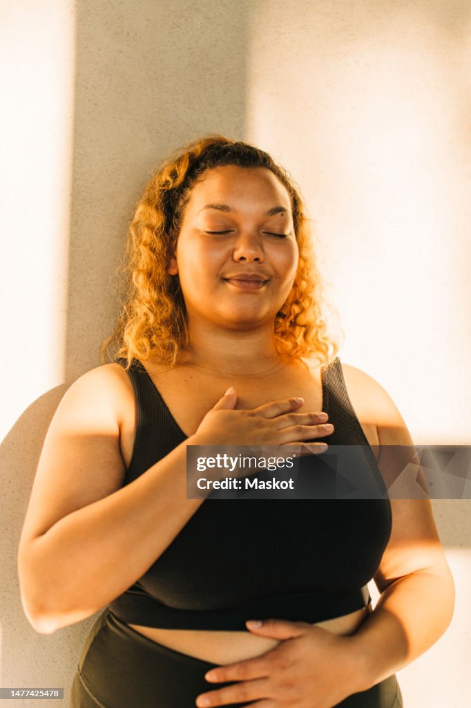 Smiling woman with eyes closed standing against wall