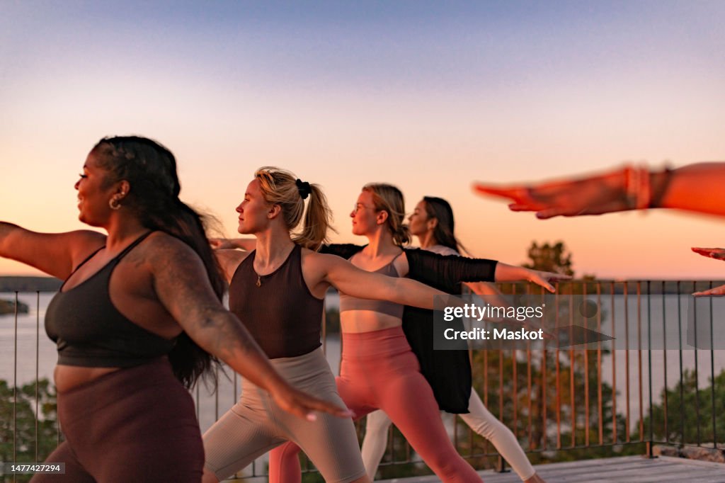 Female friends doing yoga on patio at sunset