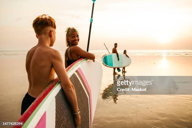 family with paddleboards walking towards sea during sunset at beach - tourist mother father child thailand stock pictures, royalty-free photos & images