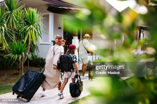 family with wheeled luggage walking on footpath while arriving at resort during vacation - wheeled luggage stock pictures, royalty-free photos & images