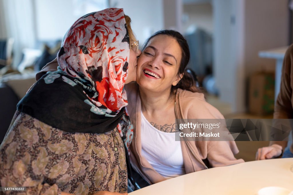 Mature woman kissing daughter with paraplegia sitting at home