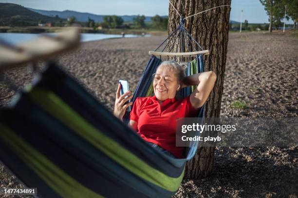 senior woman lying down in a hammock and using the phone - hammock phone stock pictures, royalty-free photos & images