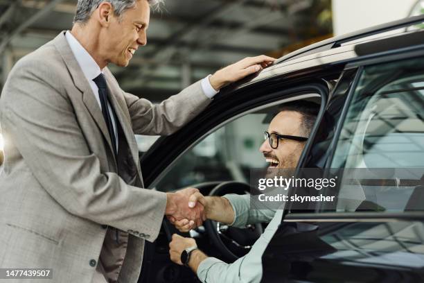 car salesperson shaking hands with his customer in a showroom. - customer test drive stock pictures, royalty-free photos & images