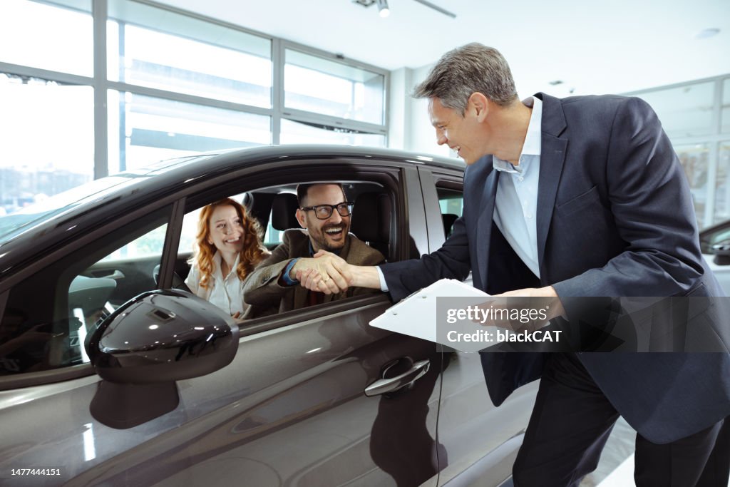 Mature sales agent helping adult couple to choose a new car in modern car showroom