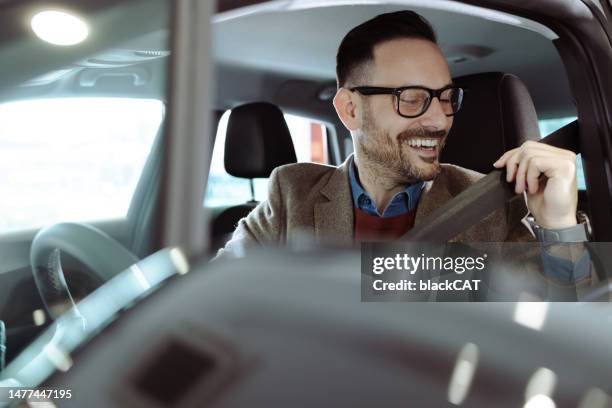 smiling man puts on a seat belt in a car - test drive stock pictures, royalty-free photos & images