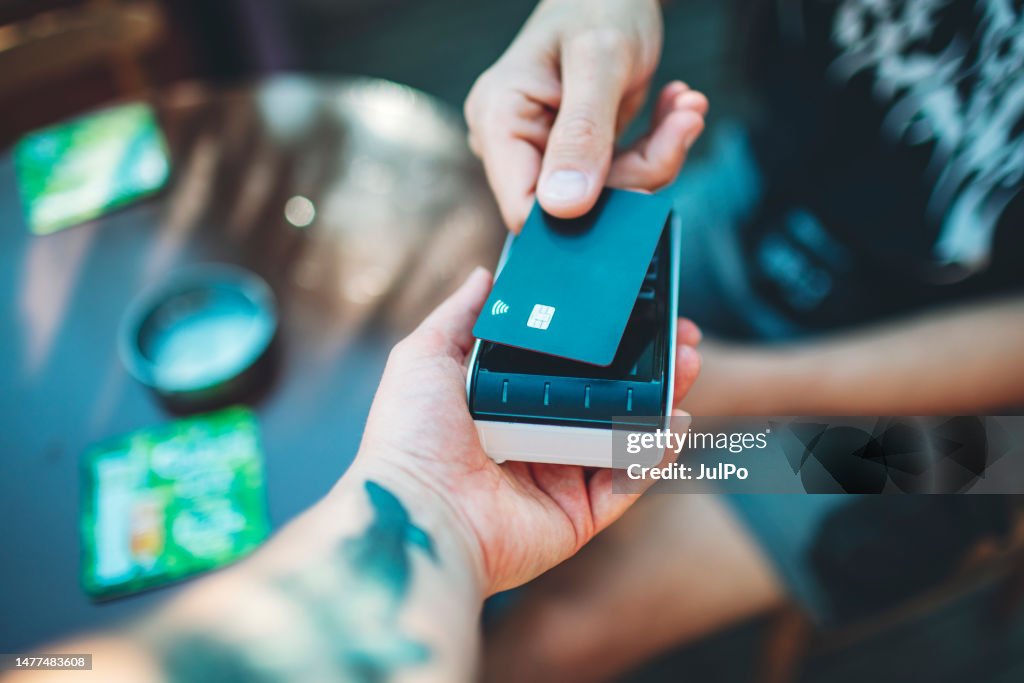 Adult man paying with credit card at cafe, close-up of hands with credit card and credit card reader