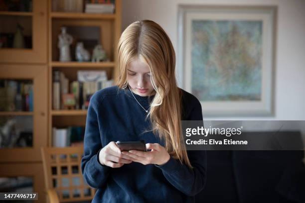 teenage girl standing in a living room, using a mobile phone. - addiction stock pictures, royalty-free photos & images