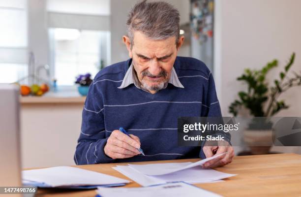 ein älterer erwachsener mann sitzt an einem tisch, auf dem papiere gestapelt sind - sozialversicherung stock-fotos und bilder