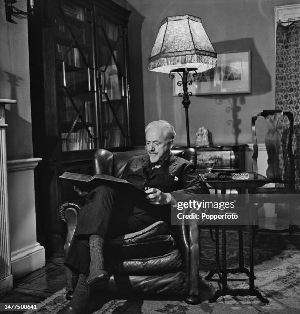 English writer and playwright Clifford Bax reads one of the many books that comprise his collection of first editions in the study library of his...