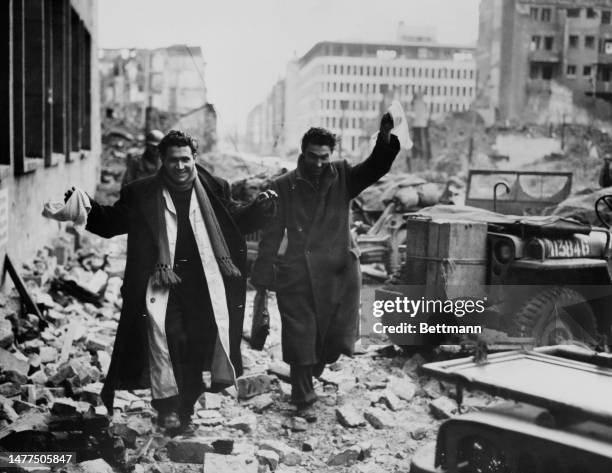 Smiling and waving white handkerchiefs, two German civilians walk towards American lines in the ruined city of Cologne on March 13th, 1945.