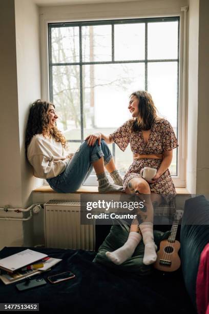 two friends laughing together on window sill - lgbtq  and female domestic life fotografías e imágenes de stock