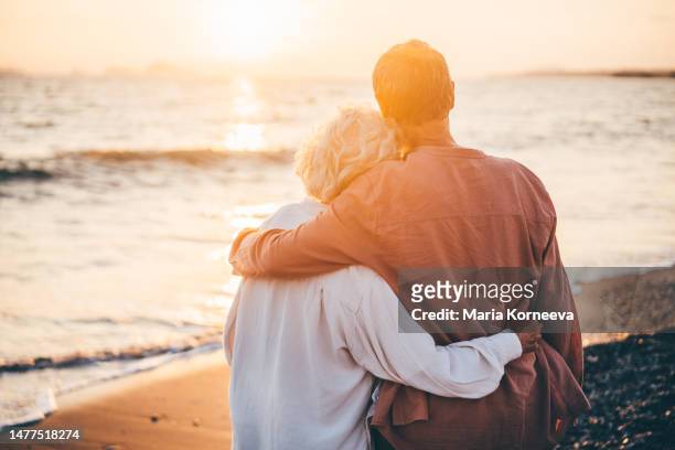 happy mature couple enjoying beautiful sunset at the beach. retirement vacation concept. - mature couple stockfoto's en -beelden