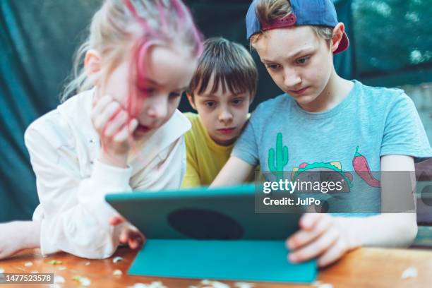 three children playing games at digital tablet - alpha stock pictures, royalty-free photos & images