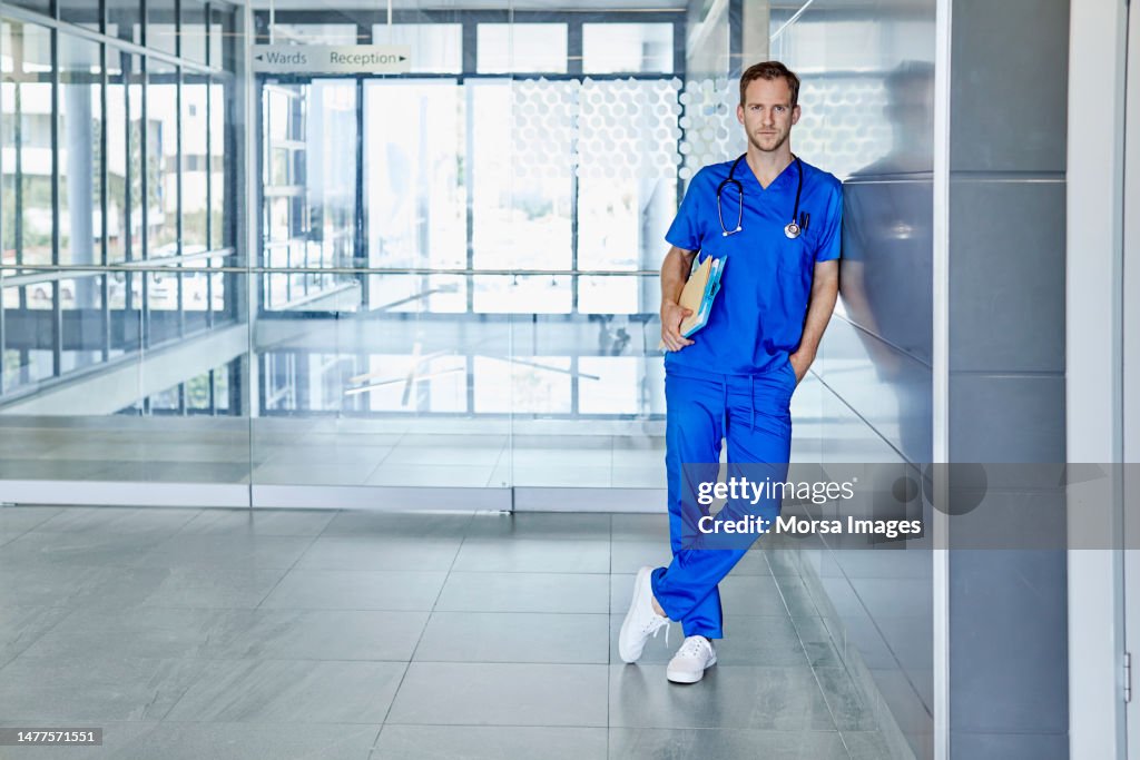 Male surgeon with medical records leaning on wall