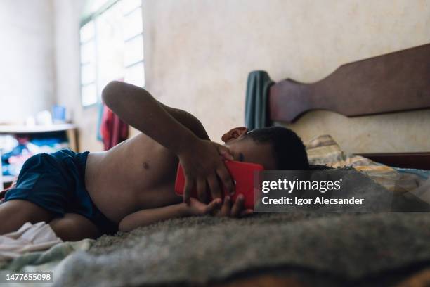 boy watching on cell phone in bed - zuid amerikaanse volksstammen stockfoto's en -beelden
