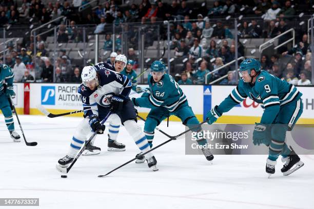 Kevin Stenlund of the Winnipeg Jets is defended by Jacob Peterson and Jacob MacDonald of the San Jose Sharks in the first period at SAP Center on...