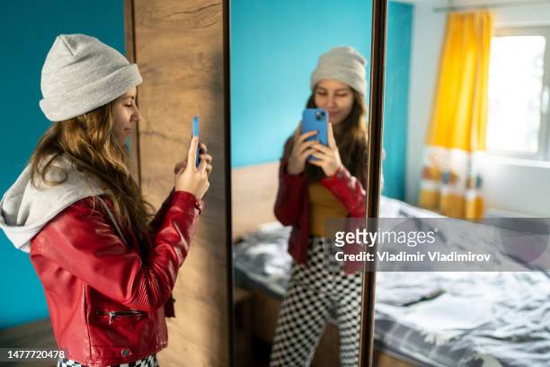 a young woman with a cell phone in front of a large mirror - girl in mirror stockfoto's en -beelden