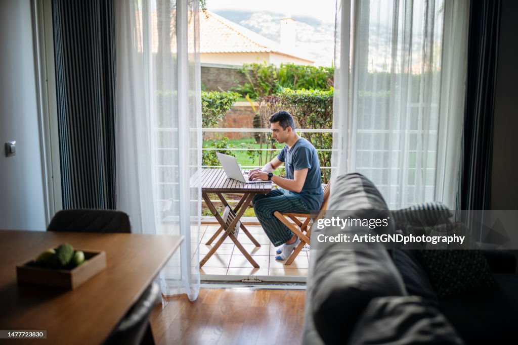 Homem trabalhando no laptop e relaxando na varanda.