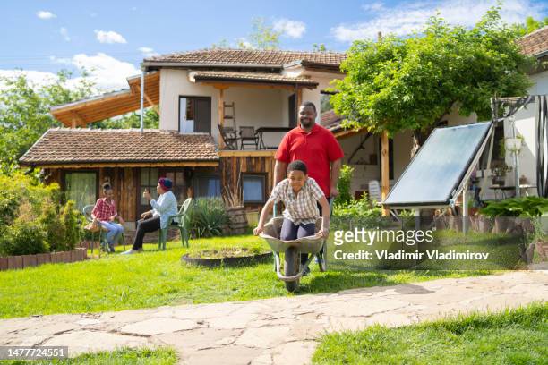 afro-american dad is driving his son in a whellbarrow - jamaican ethnicity imagens e fotografias de stock