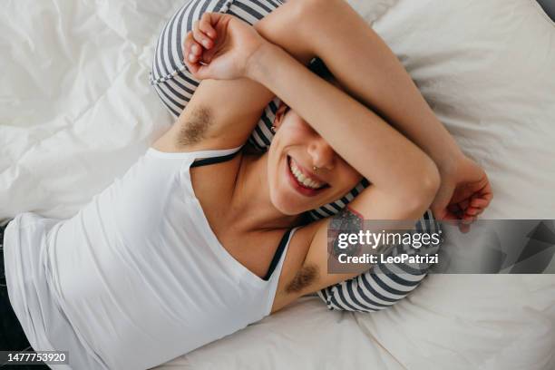 happy young woman with short hair lying on the bed - female hairy arms stock pictures, royalty-free photos & images