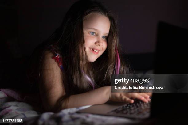 happy laughing girl typing on a laptop keyboard on a bed in the dark - addiction mobile and laptop stock-fotos und bilder