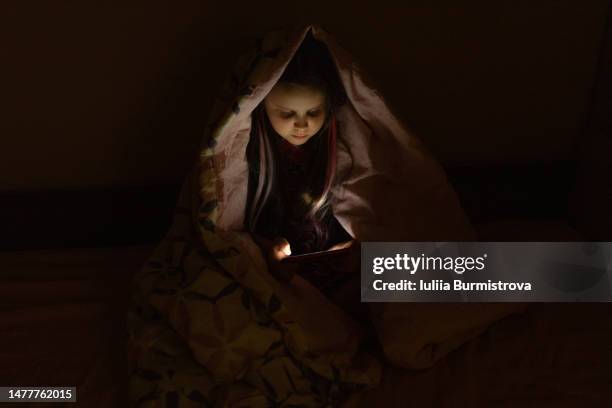 a girl sitting on a bed and holding a mobile phone in her hands in the dark at night yes - teenager girl blanket stockfoto's en -beelden