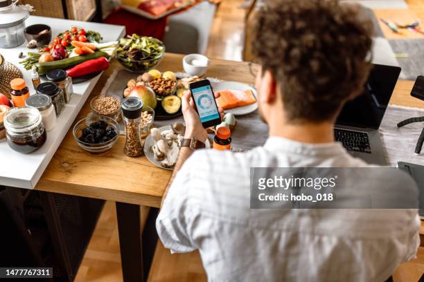 junger mann, der die nahrungsaufnahme mit einer mobilen app zu hause verfolgt - culinary stock-fotos und bilder