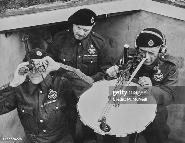 Three members of the Royal Observer Corps scan the sky with a post plotting instrument and binoculars searching for German Luftwaffe aircraft from...
