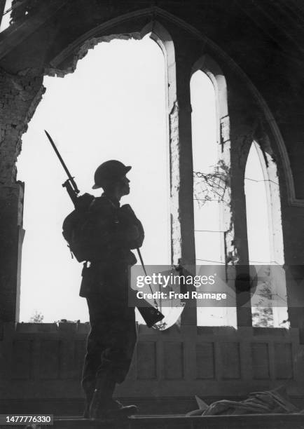 Soldier from the 51st Surrey Battalion Home Guard is silhouetted against the bomb shattered window of the Baptist Chapel in Kingston Road following...