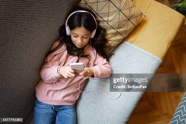 schoolgirl lying on the sofa, listen to music while using mobile phone - lying on back girl on the sofa stock pictures, royalty-free photos & images