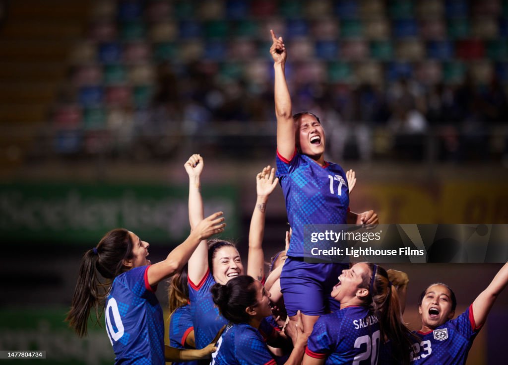 Celebrating women soccer players raise up their star player after winning the final in an international cup