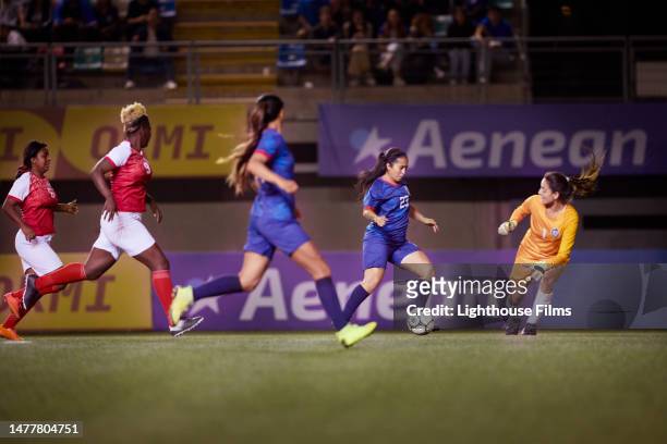 professional female football player tries to maneuver past goalkeeper and score a goal - international race stock pictures, royalty-free photos & images