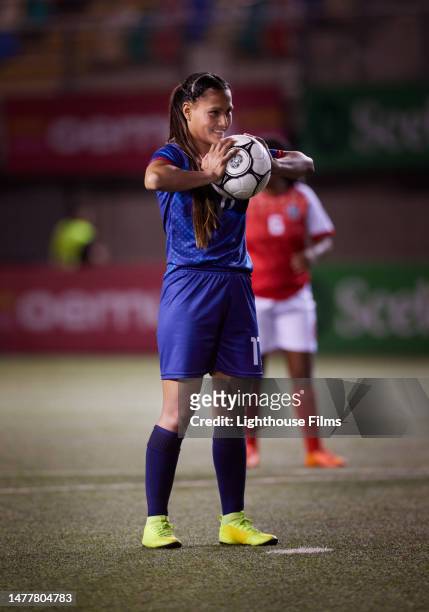 athletic female soccer player smiles in anticipation as she squeezes a soccer ball standing on the penalty spot - fifa world cup pre tournament stock pictures, royalty-free photos & images