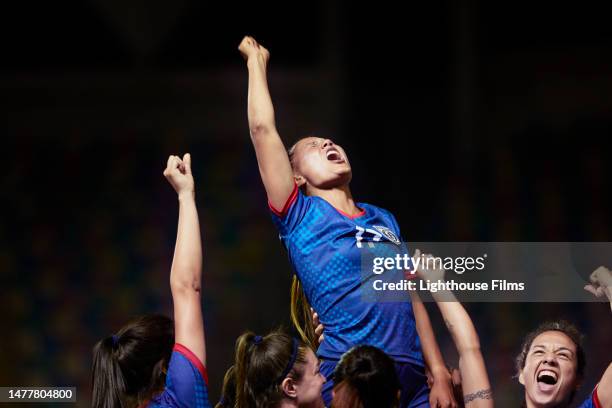 team of women soccer players raise their star teammate as they all shout in excitement - team encouragement stock pictures, royalty-free photos & images