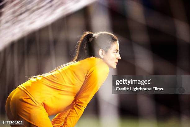 professional female soccer goalie bends her back and intently looks out at the field - woman goalie stock pictures, royalty-free photos & images