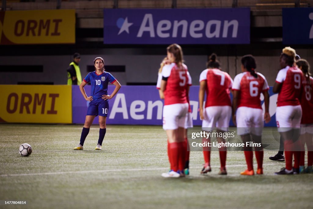 Confident #10 professional female soccer player waits to take free kick as a the opposing team prepares their wall to try and block the shot