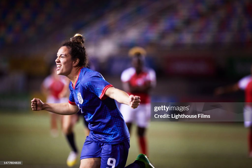 Ecstatic female soccer player pumps her firsts and runs to her teammates as she celebrates scoring a goal from a penalty kick