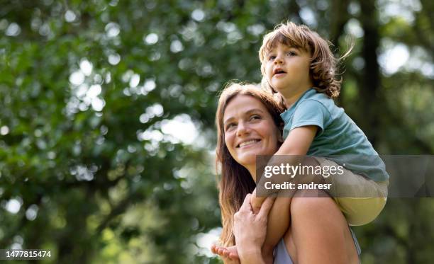 madre feliz cargando a su hijo sobre sus hombros en el parque - padre e hijas fotografías e imágenes de stock