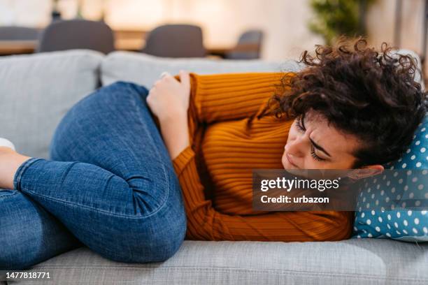 young woman having period cramps at home - appendicitis imagens e fotografias de stock