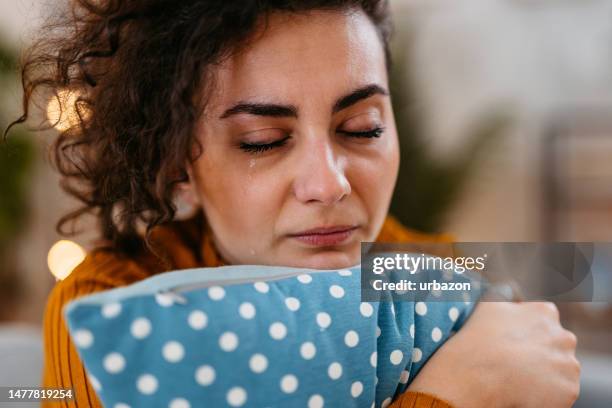 jeune femme triste étreignant un oreiller et pleurant à la maison - larme photos et images de collection