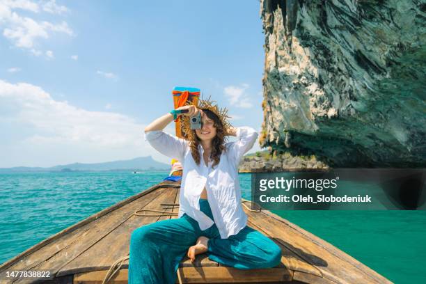 cheerful woman traveling with thai taxi boat and photographing with point and shoot camera - young woman beach stockfoto's en -beelden