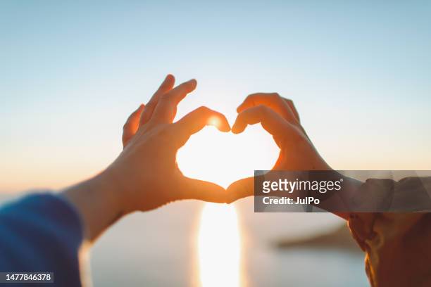 two female friends making heart shape of hands at sunset at the sea - make stockfoto's en -beelden