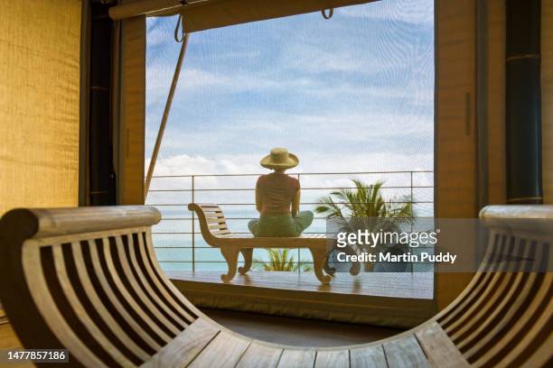 female tourist admiring sea view while relaxing on decking of tented villa, at eco friendly luxury glamping resort, at dawn - health spa stock pictures, royalty-free photos & images