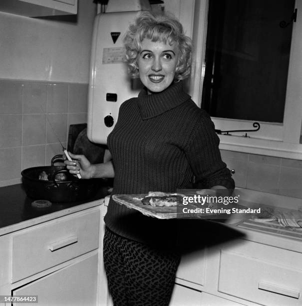 British actress Bernadette Milnes holds a chopping board and knife in a kitchen, January 22nd 1959.